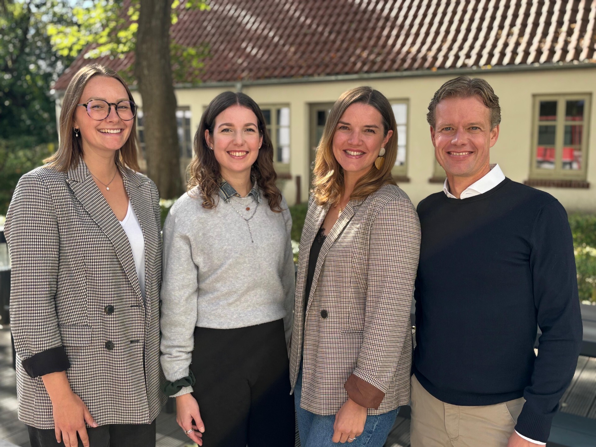 Vier Personen stehend, lächeln in Kamera